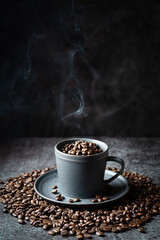 Gray cup full of steaming coffee beans on a dark gray stone background