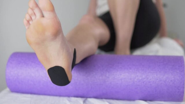 The woman makes a pre-exercise to strengthen the ankle on the bolster. Exercise in a medical center, close-up of the legs
