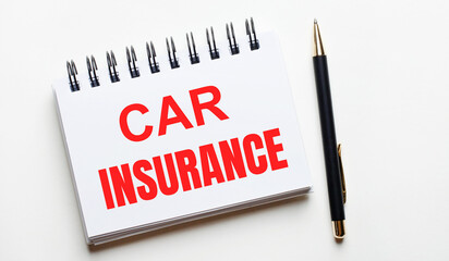 On a light background, a white notebook with are words CAR INSURANCE and a pen.