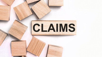 On a light background, wooden cubes and a wooden block with the text CLAIMS. View from above