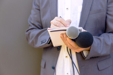 Journalist at media event or news conference, holding microphone, writing notes. Broadcast...