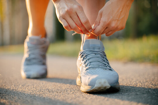 Close-up of hand tying shoelaces ready to run on the road.Gray sports sneakers on the background of the road. - Powered by Adobe