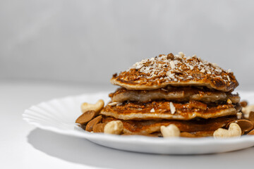 Healthy breakfast; close-up of homemade vegan pancake with raw cashew and almond nuts in white plate.