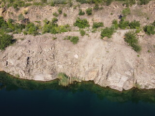 Rocky shore of the Radon Lake on a sunny summer morning. Aerial view of an old flooded granite quarry. A picturesque pond.