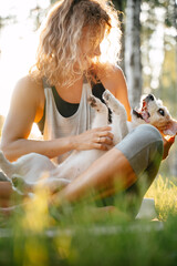 Cheerful young girl playing with pet dog while sitting on a meadow in sunlight.