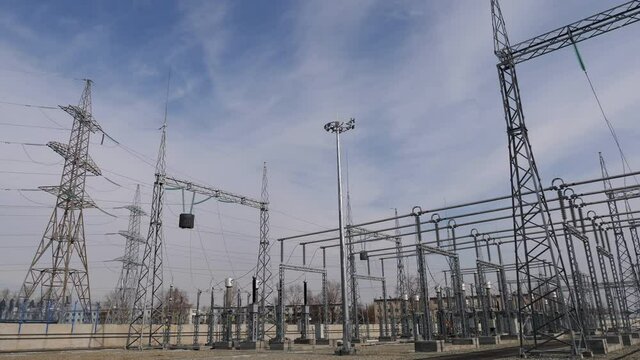 Lacy towers with electricity transmission lines installed at contemporary distribution substation under blue sky with clouds