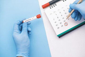  holding blood test tube and marking date on calendar 