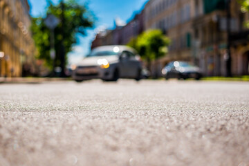 Summer in the city, the headlights of an approaching car on the street with trees. Close up view from the asphalt level