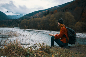 woman near the river in the mountains with a backpack on her shoulders are resting in the autumn forest