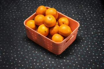 A wicker basket full of fresh orange fruits, isolated on a blue and white dotted background.