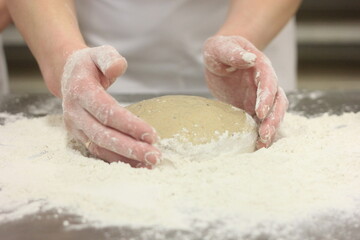 Fototapeta premium Woman's hands kneading the bread dough. Making dough by female hands on wooden table