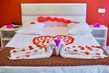 Twisted towels in the shape of a swan and rose petals in the shape of a heart. Made bed at the hotel
