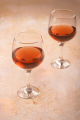 Two wine glasses with dark red alcoholic beverage on a beige colored surface