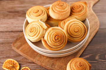 Fototapeta premium Several cinnamon buns in a beige bowl on wooden board on wooden table