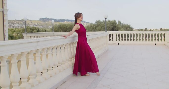 Giovane ragazza modella con vestito rosso cammina su una balconata