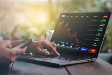 A business man is checking daily online stock market prices through a laptop at home with graphs...