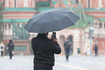 Man with umbrella taking photos on the Red Square in Moscow during rain on background of St. Basil's Cathedral