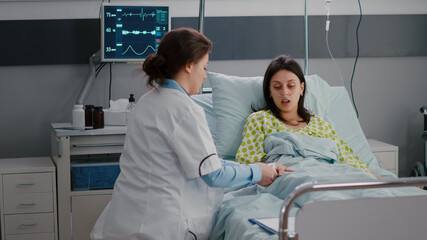 Surgeon doctor monitoring hospitalized sick woman during cardiology appointment in hospital ward putting medical oximeter checking pulse expertise. Patient resting in bed waiting disease treatment