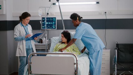 Medical practitioner doctor checking sick woman monitoring disease symptom during recovery appointment in hospital ward. Patient resting in bed while assistant putting oximeter