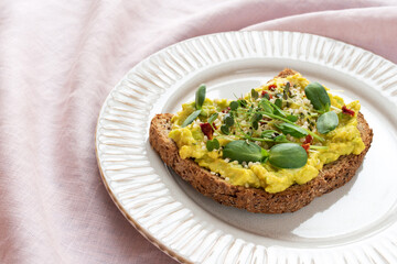 Vegan toast with avocado, microgreens and hemp seeds on a plate and pink tablecloth