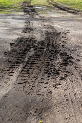 Car tire imprints in black earth and grass in wet mud with puddles and sand. Sunny spring.