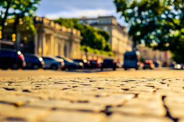 Summer in the city, the sunlit empty old street paved with stone next to the road on which cars are...