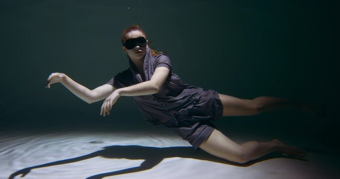Falling asleep. Young beautiful woman wearing pyjamas, eye mask sinking deep under water in swimming pool slow motion.