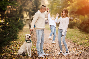 Fototapeta premium Happy beautiful family with dog labrador is having fun together walking the in park.