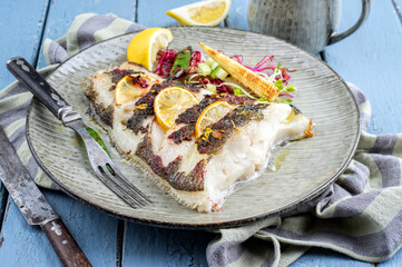 Modern style traditional roasted halibut fish filet with lettuce and lemon slices served as...