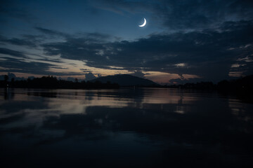 See the Islamic moon in the night sky. The evening sky and the vast river in darkness are beautiful. The crescent moon concept, the symbol of Islam, begins the month of Ramadan, eid al fitr