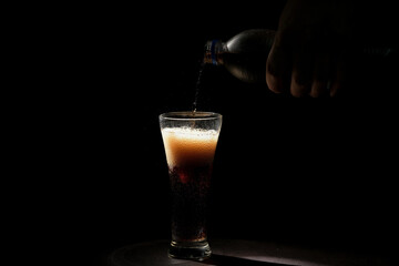 Cola pouring from bottle into glass on black background.