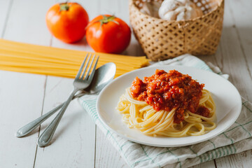 Delicious homemade Spaghetti pasta with tomato sauce and minced meat served on a white plate with ingredient on white wooden background. Italian food. Homemade food.