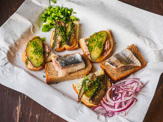 Sandwiches with herring, pickles, onion, sprats on white papper