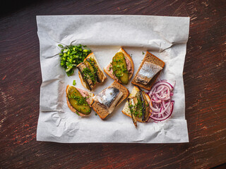 Sandwiches with herring, pickles, onion, sprats on white papper
