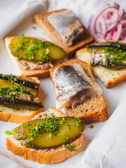 Sandwiches with herring, pickles, onion, sprats on white papper