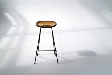 Wooden chair standing in the middle room with hard window frame shadows on white floor