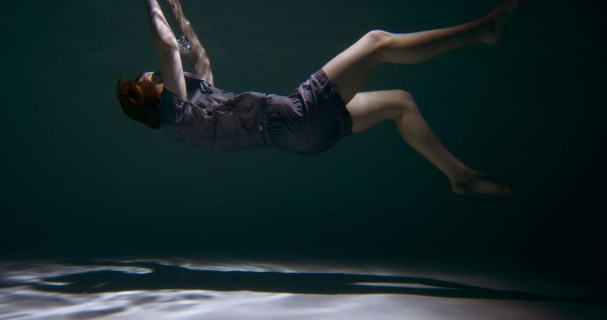 FALLING ASLEEP. Incredible view of young beautiful woman in pyjamas, sleep mask sinking under water dreaming slow motion
