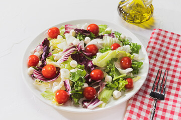 The Mediterranean diet. Healthy food composition with salad with herbs, cherry tomatoes, mozzarella and olive oil on a white plate with fork on a white background. The concept of simple healthy food