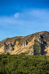 moon over green mountain hills with cliffs during day