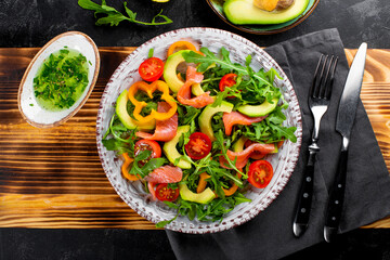 Fresh summer vegetable salad with arugula, tomatoes, bell peppers, avocado and salmon on a plate top view