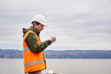 geologist or mining engineer examines a sample of a mineral from a talus on a river bank