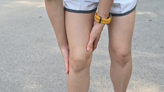 Close up of runner woman holding her knees and doing knee massage while she having suffering from overtraining.