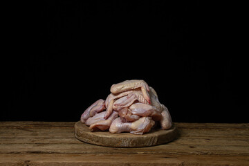 Raw chicken wings on a black background. Fresh chicken meat. Heap of raw chicken wings on a wooden board.