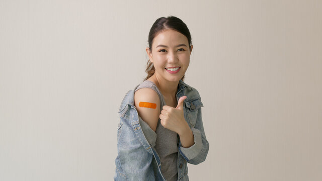 Young attractive beautiful asia female or teenage receive covid-19 anti virus vaccine in campaign vaccination safe life happy smile cheerful with blue, yellow, pink bandage on arm with copy space.