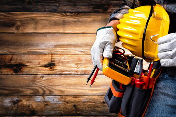 Electrician technician with tool belt on rustic wooden background. Electricity.