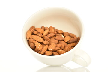 Several grains of peeled raw, organic almonds with white ceramic dishes, close-up, isolated on white.
