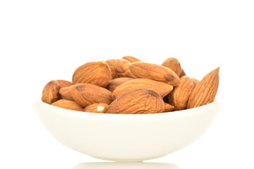 Several grains of peeled raw, organic almonds with white ceramic dishes, close-up, isolated on white.