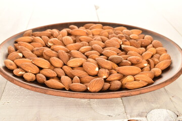Several grains of peeled raw, organic almonds on a clay plate, close-up, on a wooden table.