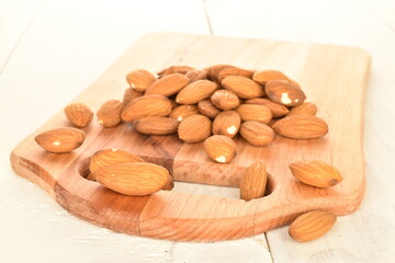 Several grains of peeled raw, organic almonds on a wooden cutting board, close-up, on a wooden table.