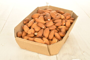 Several grains of peeled raw, organic almonds in a paper plate, close-up, on a wooden table.